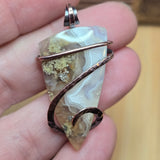 Pendant with agate stone and copper wire wrap held in a hand against a blurred background