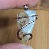 Pendant with a copper wire wrap held between fingers against a wooden background