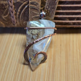 Moss agate pendant with silver wrap on wooden surface