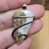 Pendant with a natural stone and copper wire design held in a hand.