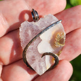 Hand holding a crystal pendant with a natural rock background