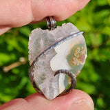 Hand holding agate pendant in sterling silver against green blurred background