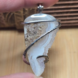 Moss agate pendant held between two fingers against natural background