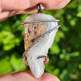 Moss agate pendant with crystal edge held against blurred green background