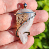 Moss Agate pendant with crystal edge held in hand against blurred green background