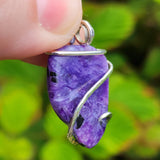 Purple stone pendant with silver wire wrapping held by a hand against a green leafy background