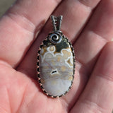 Pendant with a patterned stone held between fingers