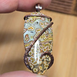 Hand holding a unique stone pendant with floral patterns and copper accents.