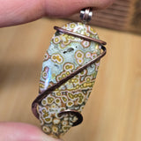 Pendant with floral patterned stone held by a hand against a blurred background