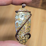 Hand holding a unique stone pendant with intricate patterns against a wooden background