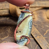 Hand holding a stone pendant with copper wire wrapping on a textured surface
