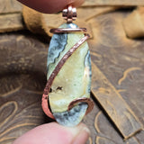 Hand holding a stone pendant with copper accents on a wooden surface