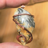 Jewelry with a stone and copper wire wrapping held between fingers against a blurred background