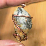 Pendant with stone and copper wire wrapping held by a hand against a blurred background