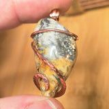 Close-up of a stone pendant with copper wire wrapping held between fingers against a blurred background