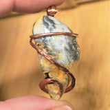 Hand holding a stone pendant with copper wire wrapping against a blurred background