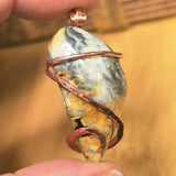 Pendant with a stone and copper wire wrapping held by a hand against a blurred background