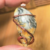Pendant with stone and copper wire wrapping held by a hand against a blurred background