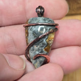 Jewelry pendant with stone and copper wire wrapping held between fingers