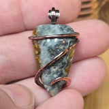 Pendant with stone and copper wire wrapping held between fingers