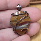 Jasper pendant with copper wire wrapping held between fingers