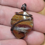 Close-up of a stone pendant with copper wire wrapping held between fingers.