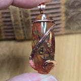 Copper-wrapped pendant held between fingers with a blurred background