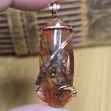Hand holding a copper-wrapped stone pendant with a blurred background