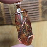 Pendant with marbled stone and copper wire wrapping held by a hand against a blurred background