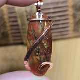 Jewelry pendant with a copper wire wrap held by a hand against a blurred background