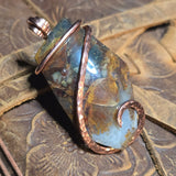 Copper-wrapped stone pendant on a textured surface