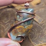 Jasper pendant with copper wire wrapping held by a hand against a blurred background