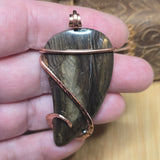 Hand holding a stone pendant with copper wire wrapping on a wooden surface