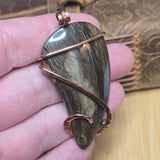 Hand holding a stone pendant with copper wire wrapping against a textured background