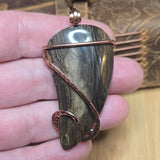 Hand holding a stone pendant with copper wire wrapping on a wooden surface