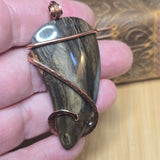 Hand holding a stone pendant with copper wire wrapping against a blurred background