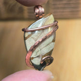Close-up of a stone pendant with copper wire wrapping held between fingers.