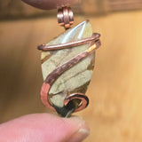 Jewelry pendant with stone and copper wire wrapping held between fingers against a blurred background
