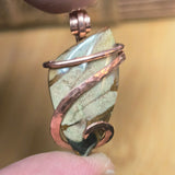 Jewelry pendant with stone and copper wire wrapping held by a hand against a blurred background