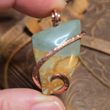 Hand holding a pendant with a picture Jasper design and copper accents.