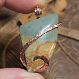 Jewelry pendant with stone and copper accents held between fingers on a wooden surface