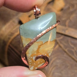 Picture Jasper pendant with copper accents held between fingers on a textured surface