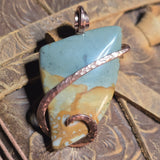 Jewelry pendant with picture jasper stone and copper accents on a textured surface