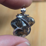 Close-up of a silver pendant with a dark stone held between fingers against a blurred background