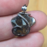 Close-up of a silver pendant with a textured stone on a finger