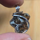 Close-up of a metallic pendant held between two fingers against a blurred background