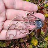 Hand holding a copper wire sculpture of a meteor against a natural background