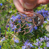 Hand holding a copper wire sculpture of a meteor against a natural background