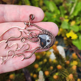 Hand holding a wire-wrapped stone pendant against a natural background