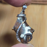 Metallic pendant held between fingers against a blurred background